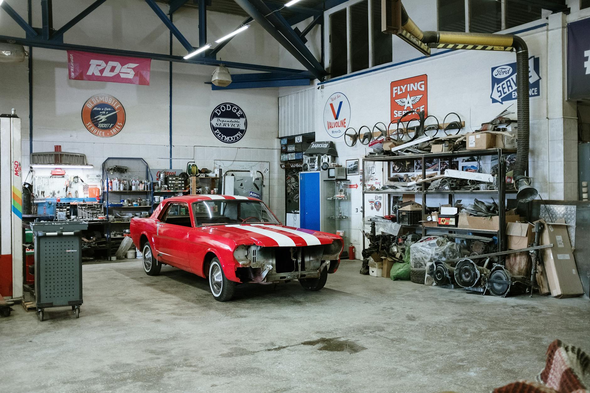 Un garage avec une voiture rouge aux bandes blanches partiellement démontée, entourée d'outils et de pièces mécaniques.